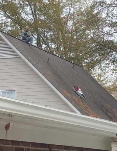 My neighbor using a blower taped to a skateboard on a rope to clean the roof