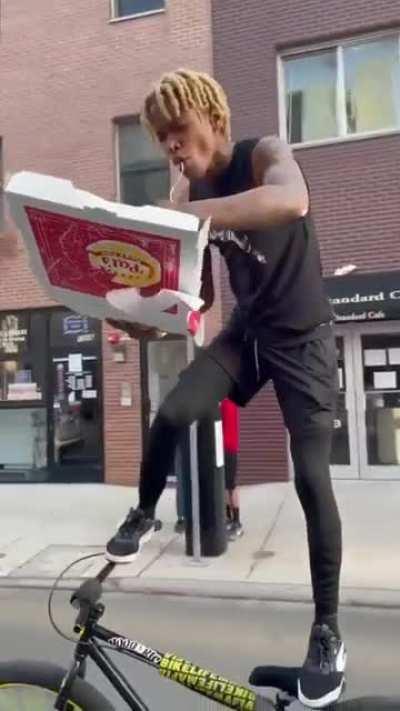 WCGW Riding a bike by standing on it, steering with one leg whilst eating pizza.