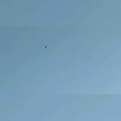 Stationary round metallic object with a helicopter circling it