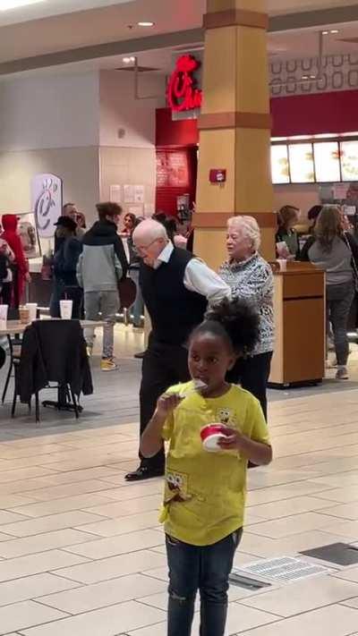 Elderly Couple Living Their Best Life, And Dancing In The Mall Food Court