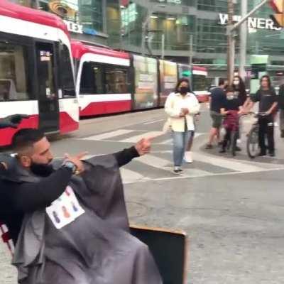 Barber cuts someone's hair in the middle of a busy intersection