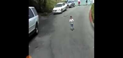 Kid falls off scooter while going down hill. Sliding across the road.