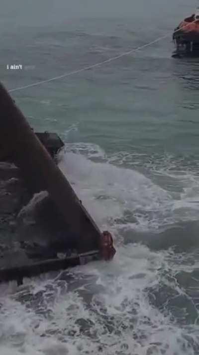 Man sits on a gigantic charcoal container that weighs slowly and heavily by the sea. It seems very dystopian and scary, just to be clear.
