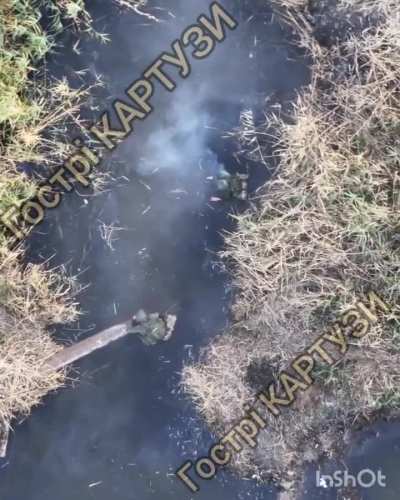 Two Russian soldiers crossing a creek are hit by a drone-dropped grenade, causing the water around the soldiers to turn red. Published August 28th, 2025.