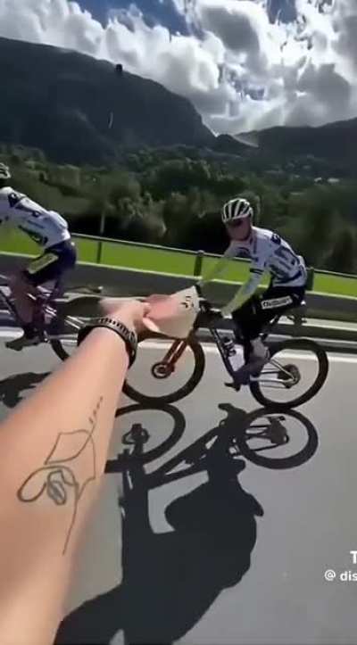 Passenger feeds cyclist riding down the road