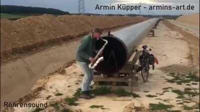 Guy playing saxophone in front of a pipeline, using its echo.