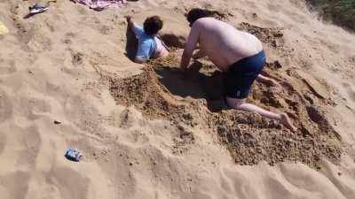 Two Bri’ish guys dig a hole while a third Bri’ish guy films them with a drone