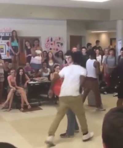 A guy that looks like Harry Potter holds his foot and jumps over his leg in a dance off competition 